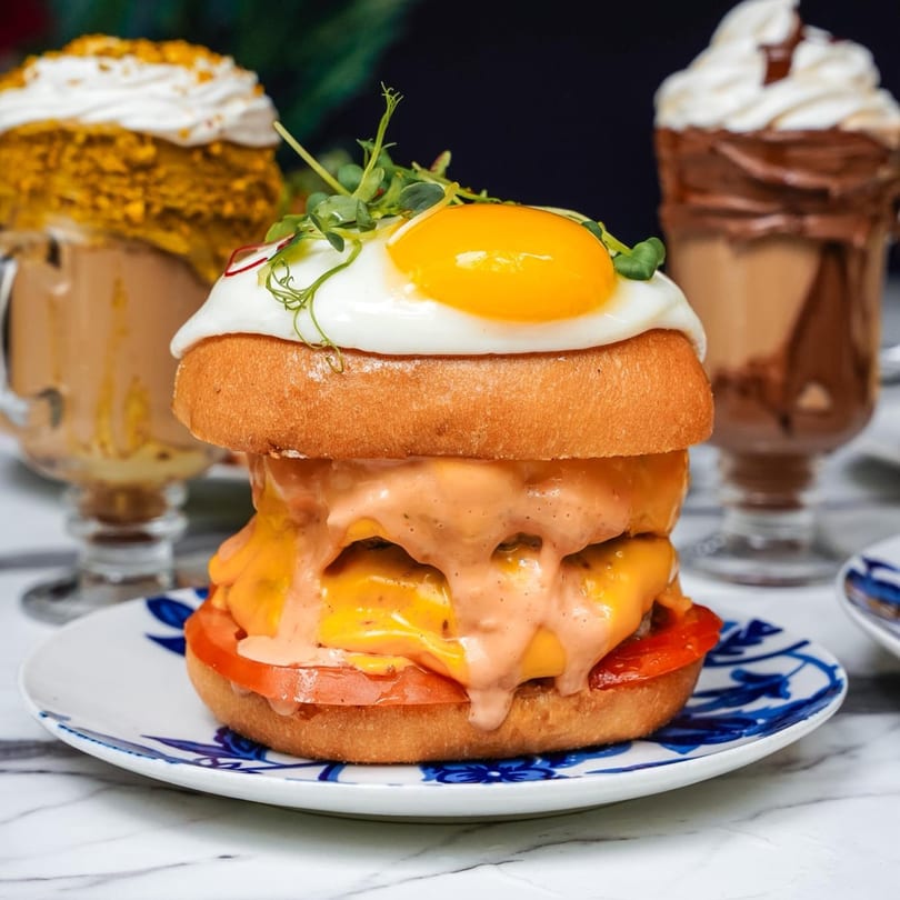 A breakfast burger with a fried egg, cheese, and sauce, served with two milkshakes.