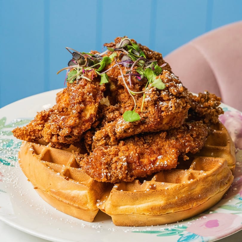 Crispy fried chicken pieces with microgreens and powdered sugar, served on a waffle.